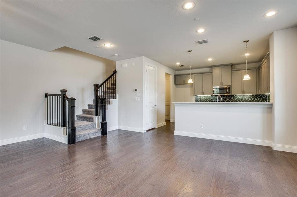 6341 Fortuna Lane, McKinney, TX 75070 Open-concept interior featuring wood-finish flooring, recessed lighting, a kitchen breakfast bar, herringbone-patterned tile backsplash, and a staircase with stained-wood handrails