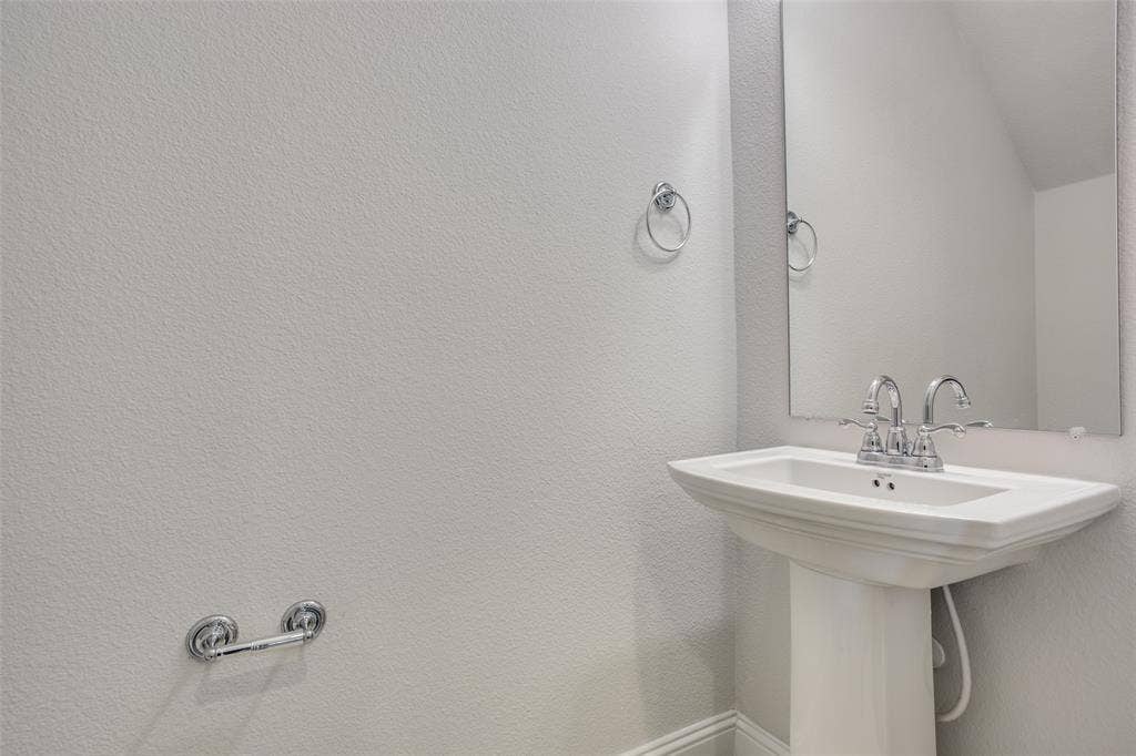 6341 Fortuna Lane, McKinney, TX 75070 Pedestal sink with a polished chrome faucet, wall-mounted mirror, and matching chrome hardware fixtures