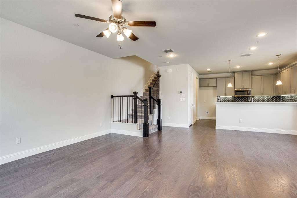 6341 Fortuna Lane, McKinney, TX 75070 Open-concept interior featuring wood-finish flooring, a kitchen with cabinetry and a breakfast bar, recessed lighting, and a staircase with a black balustrade