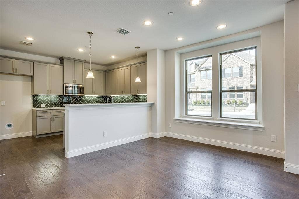 6341 Fortuna Lane, McKinney, TX 75070 Kitchen featuring wood-finish flooring, shaker-style cabinetry, a herringbone-patterned tile backsplash, pendant lighting, and a peninsula breakfast bar