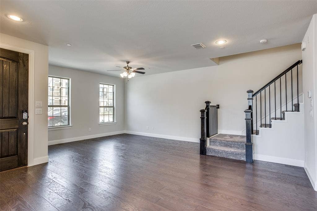 6341 Fortuna Lane, McKinney, TX 75070 Open-concept interior featuring wood-finish flooring, recessed lighting, a ceiling fan, a dark-stained wood entry door, and a staircase with a black metal railing