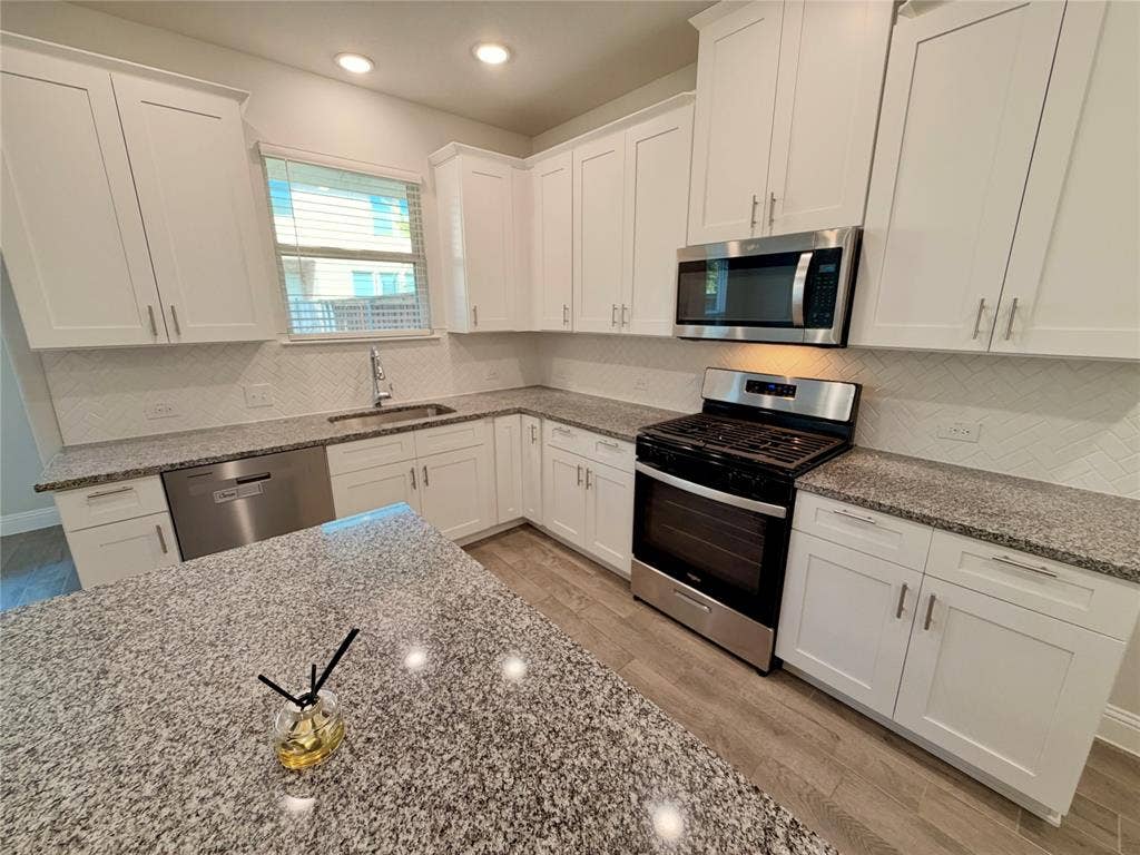 1063 Mj Brown Street, Allen, TX 75002 Kitchen featuring white cabinetry, stone-finish countertops, stainless steel appliances, a herringbone-patterned backsplash, and wood-finish flooring