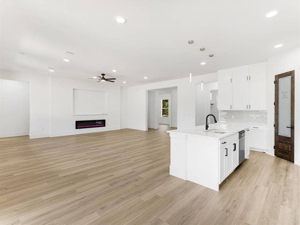 475 Loren Boyd Road, Combine, TX 75159 Open-concept interior featuring light wood-finish flooring, white cabinetry with matte black hardware, a central kitchen island with a matte black faucet, a built-in wall-mounted electric fireplace, and recessed lighting