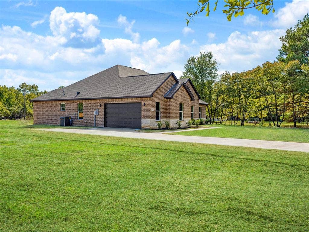 475 Loren Boyd Road, Combine, TX 75159 Brick and stone exterior featuring an attached multi-car garage, asphalt shingle roofing, and an expansive lawn on a wooded lot