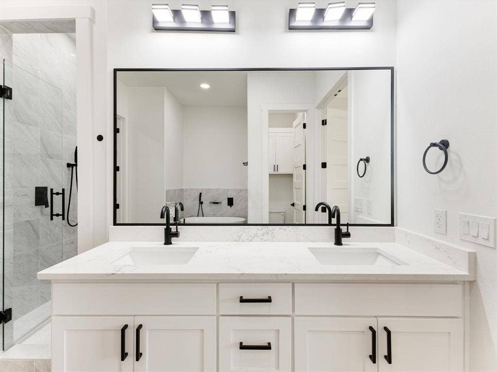475 Loren Boyd Road, Combine, TX 75159 Dual-sink vanity with white cabinetry, stone-finish countertop, matte black hardware, integrated rectangular basins, and a large rectangular mirror framed in black