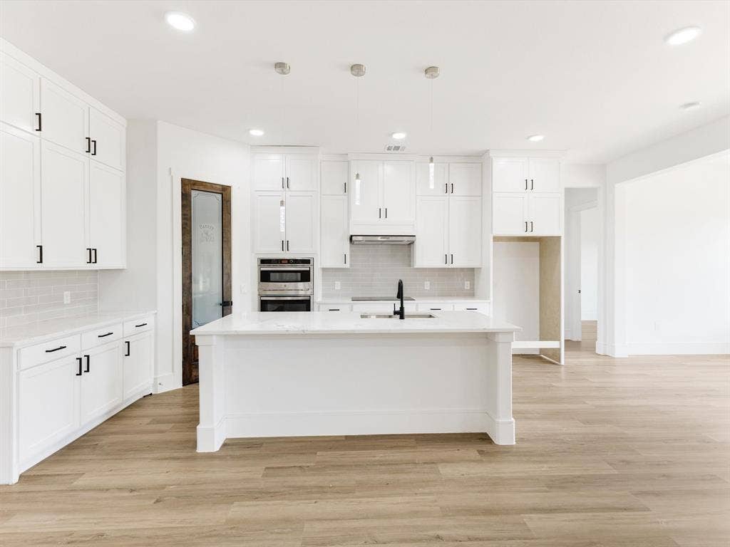 475 Loren Boyd Road, Combine, TX 75159 Kitchen featuring shaker-style cabinetry, a central island with a stone-finish countertop, stainless steel double wall ovens, wood-finish flooring, and a glass-paneled pantry door