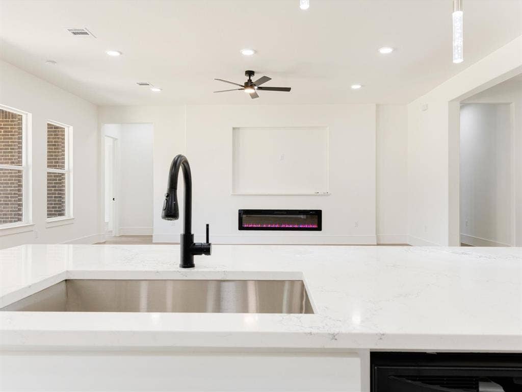 475 Loren Boyd Road, Combine, TX 75159 Kitchen featuring a large solid-surface island with an undermount stainless steel sink and a matte black pull-down faucet, complemented by a recessed wall-mounted fireplace and recessed ceiling lighting
