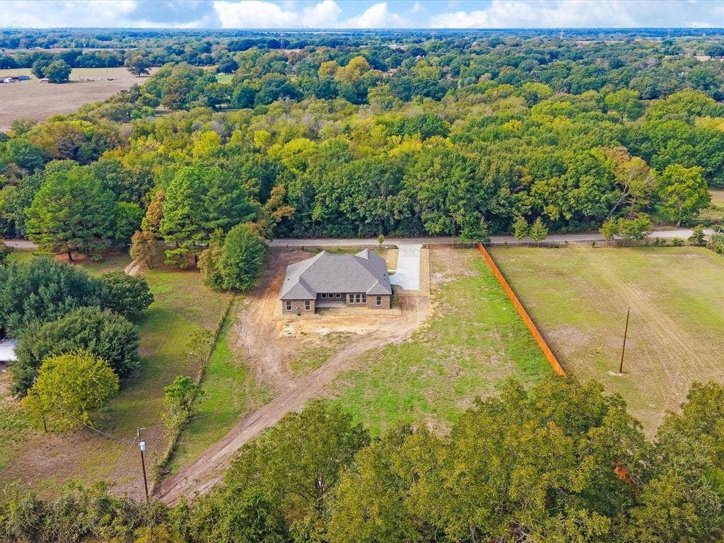 475 Loren Boyd Road, Combine, TX 75159 Single-story residence featuring a multi-gable roofline, exterior brick masonry, concrete driveway, and expansive acreage bordered by mature trees and wood fencing