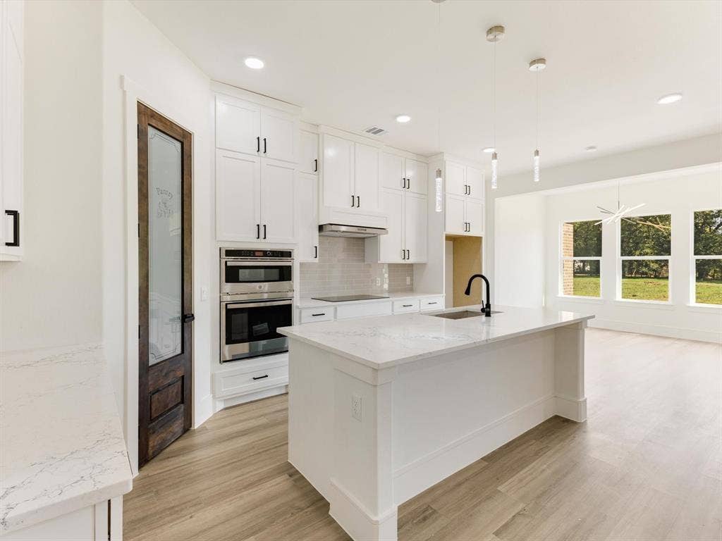 475 Loren Boyd Road, Combine, TX 75159 Kitchen featuring white shaker-style cabinetry, quartz countertops, a central island with an undermount sink, built-in double wall ovens, and a stained-wood pantry door with glass inlay