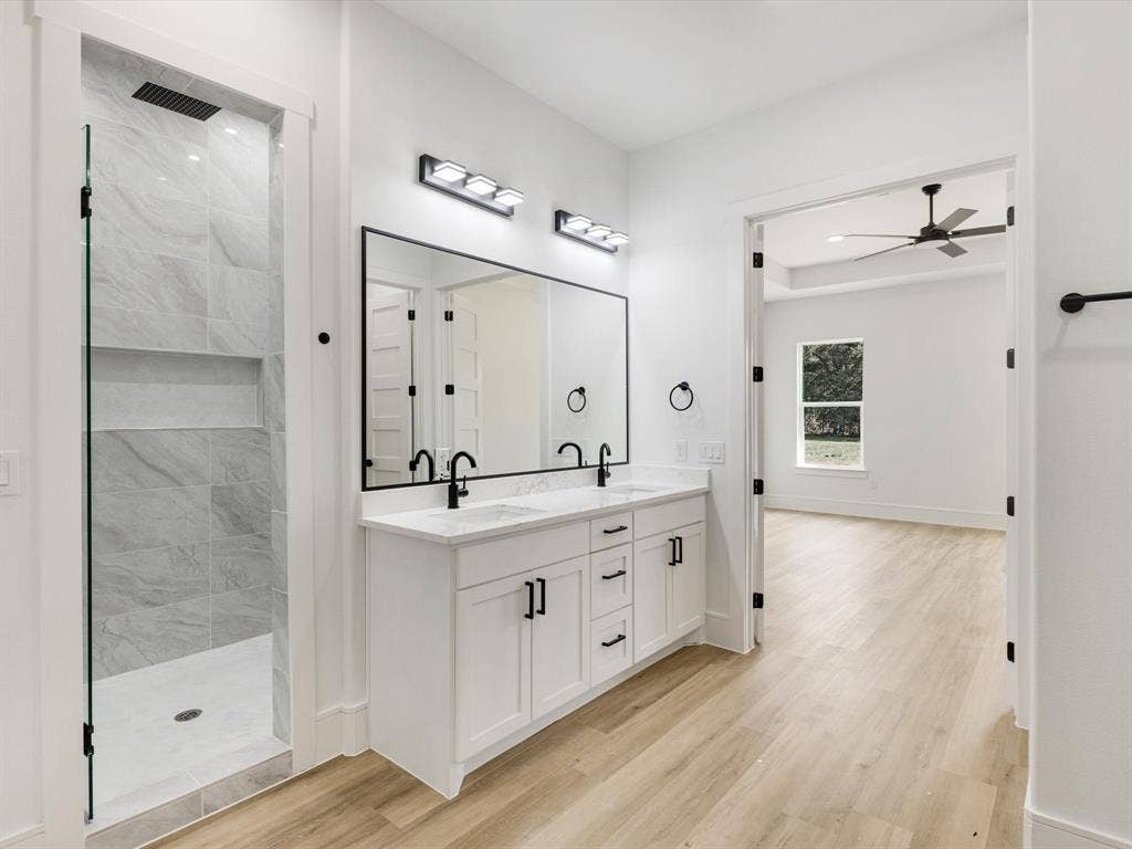 475 Loren Boyd Road, Combine, TX 75159 Double vanity featuring white cabinetry, quartz countertops, matte black fixtures, a full-width mirror, and a walk-in shower with floor-to-ceiling tile surround and recessed shelving