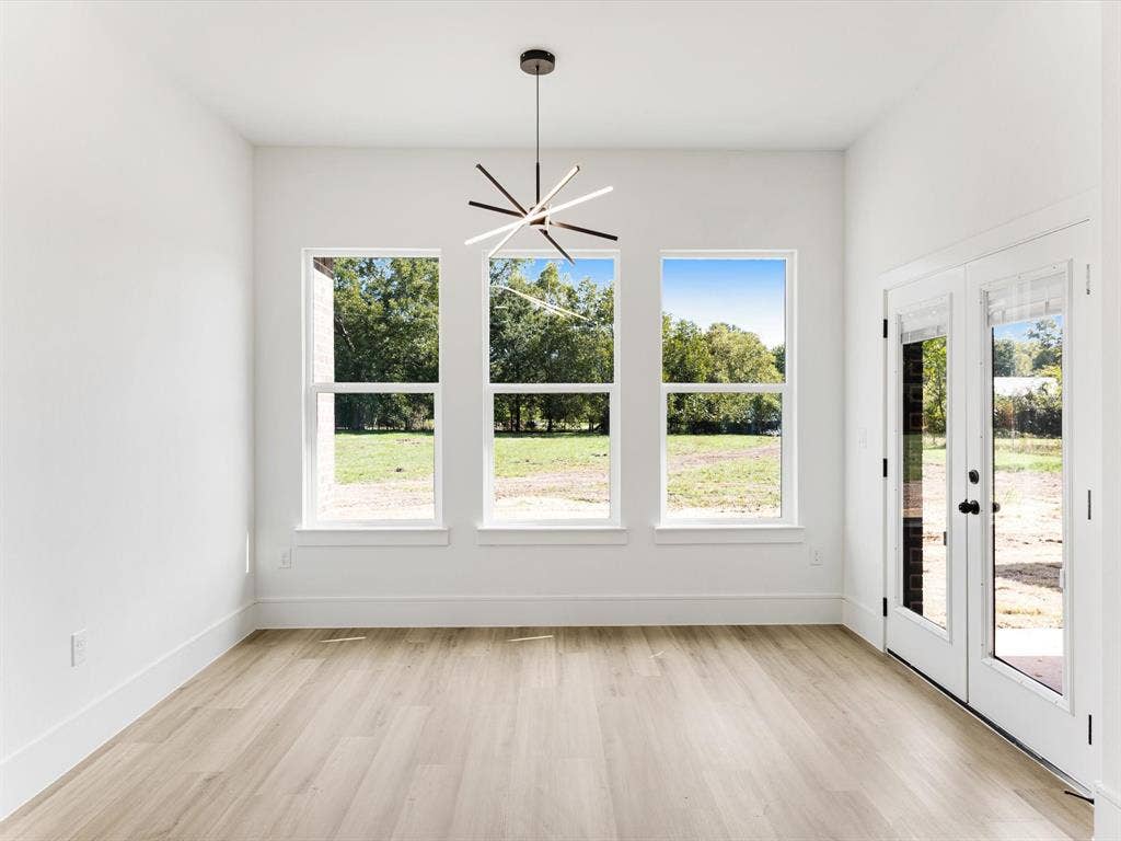 475 Loren Boyd Road, Combine, TX 75159 Modern space featuring light-toned wood-finish flooring, three vertical windows, a contemporary multi-spoke pendant light fixture, and glass-paneled double doors