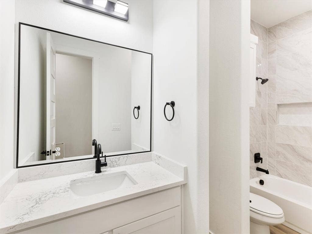475 Loren Boyd Road, Combine, TX 75159 Bathroom vanity featuring a stone-composite countertop with an integrated rectangular sink, black-finish faucet, framed wall-mounted mirror, and tile-surround tub area with a built-in recessed niche