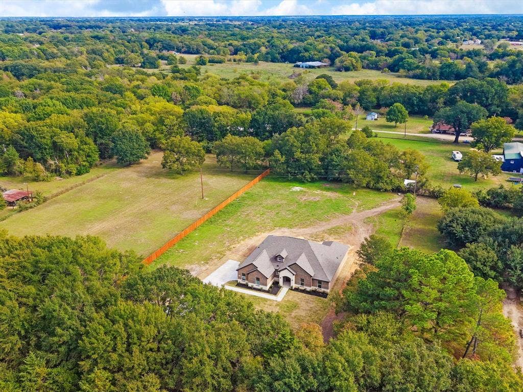 475 Loren Boyd Road, Combine, TX 75159 Aerial perspective of a multi-gabled residence featuring brick and masonry exterior finishes, surrounded by expansive acreage, mature tree clusters, and a wooden privacy fence