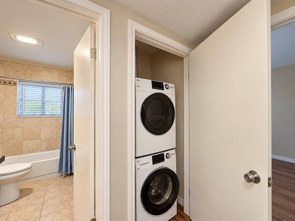 7525 Holly Hill Drive, #3, Dallas, TX 75231 Dedicated laundry closet featuring a stackable washer and dryer unit, set beside a bathroom finished with neutral wall tiling and floor tiling