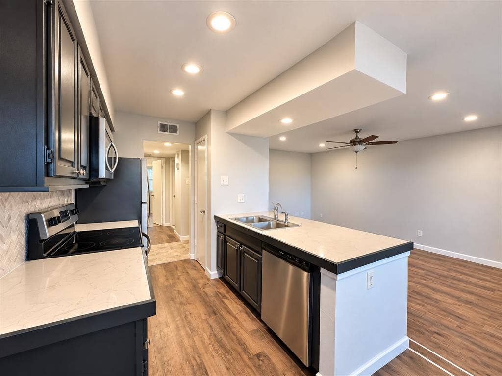 7525 Holly Hill Drive, #3, Dallas, TX 75231 Kitchen featuring dark cabinetry, stone-finish countertops, herringbone-pattern tile backsplash, stainless steel appliances, and wood-finish flooring