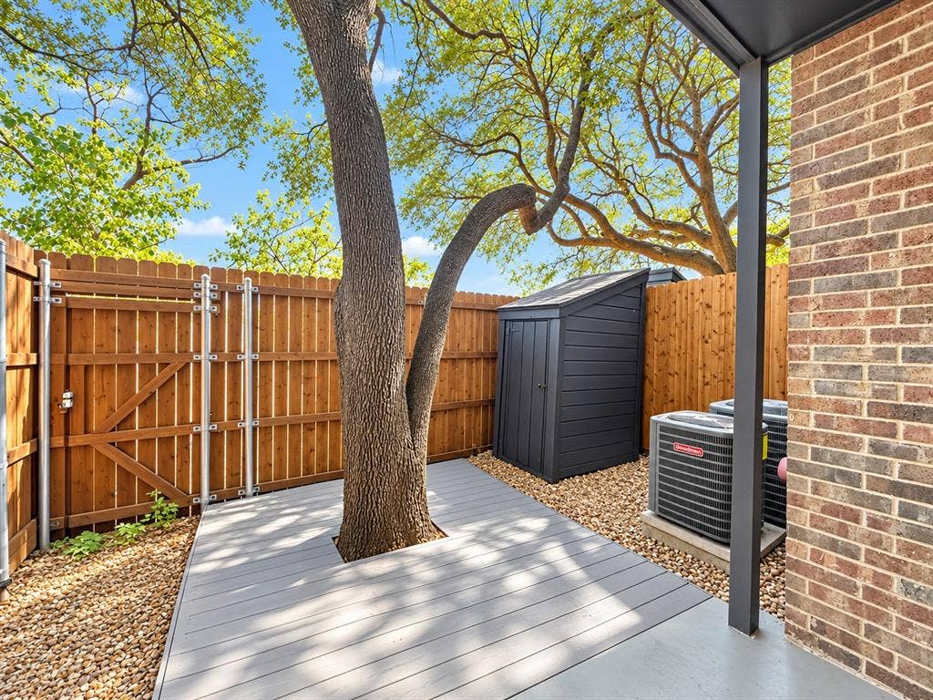 7525 Holly Hill Drive, #3, Dallas, TX 75231 Exterior space featuring a grey composite deck, wood privacy fencing, a gravel landscape, and a brick facade