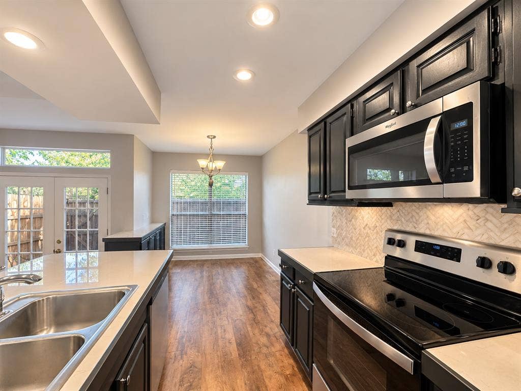 7525 Holly Hill Drive, #3, Dallas, TX 75231 Kitchen featuring dark cabinetry, stainless steel appliances, herringbone-patterned tile backsplash, quartz countertops, and wood-finish flooring
