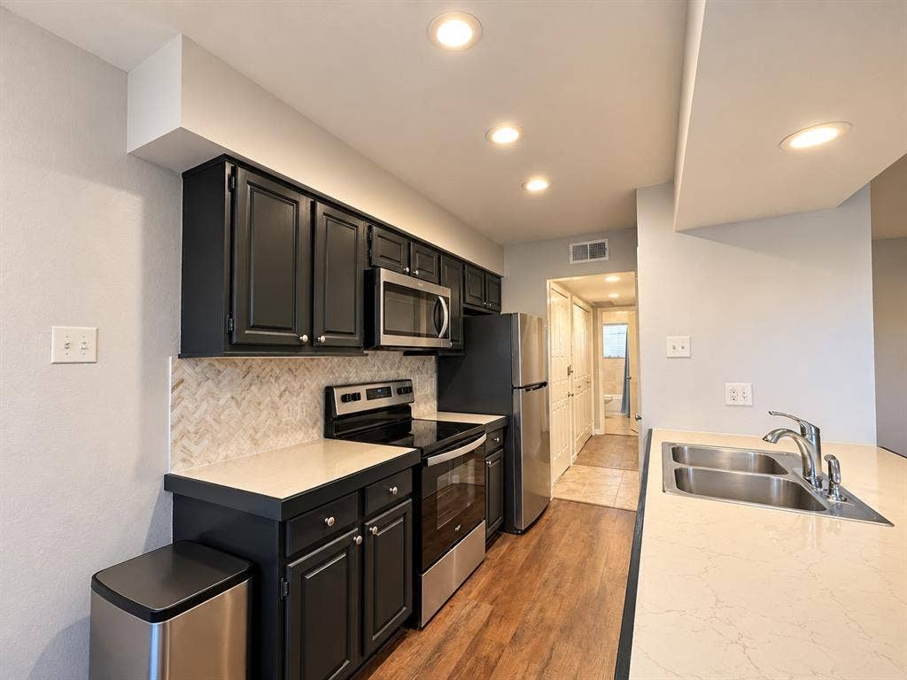 7525 Holly Hill Drive, #3, Dallas, TX 75231 Kitchen featuring dark cabinetry, stone-finish countertops, stainless steel appliances, herringbone-patterned tile backsplash, and wood-finish flooring