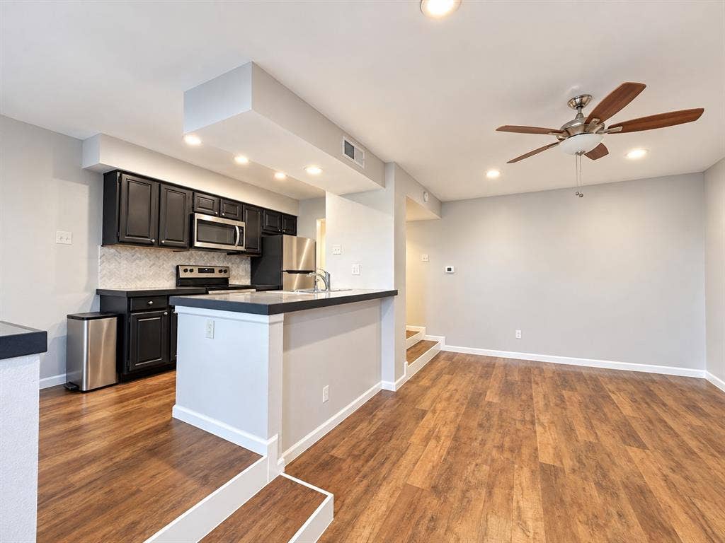 7525 Holly Hill Drive, #3, Dallas, TX 75231 Kitchen featuring dark cabinetry, solid-surface countertops, light-toned backsplash tile, wood-finish flooring, and a ceiling-mounted fan with integrated lighting