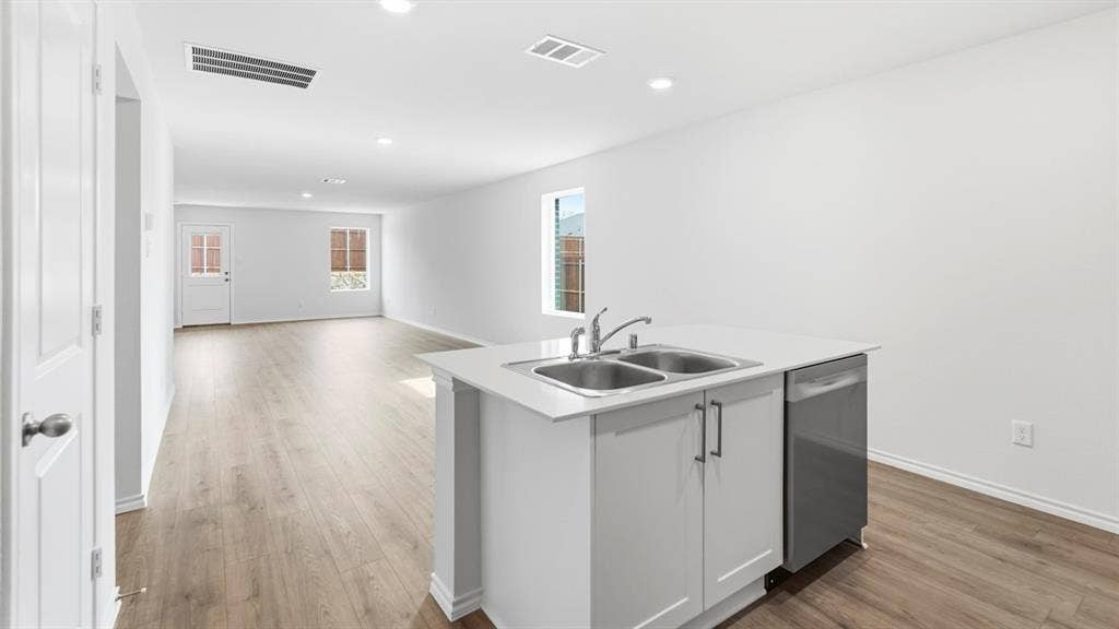 Open-concept living area with wood-finish flooring, recessed lighting, and a kitchen island featuring a double-basin sink, stainless steel faucet, and integrated dishwasher