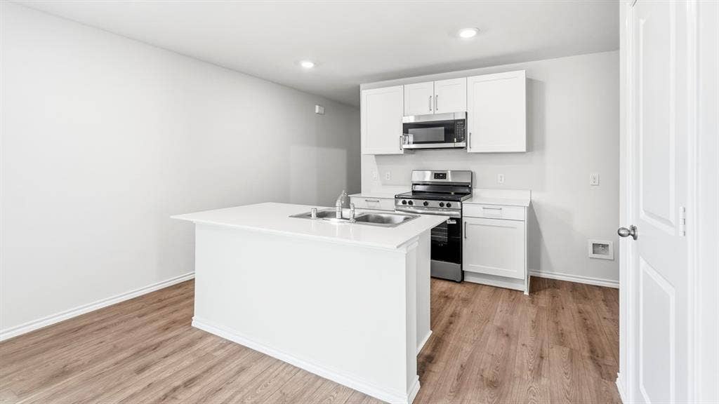 Kitchen featuring white shaker cabinetry, stainless steel appliances, a center island with an undermount double basin sink, and wood-finish flooring