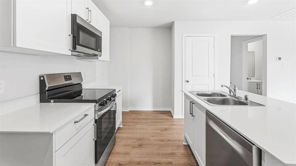 Kitchen featuring white cabinetry, light countertops, stainless steel appliances, and wood-finish flooring