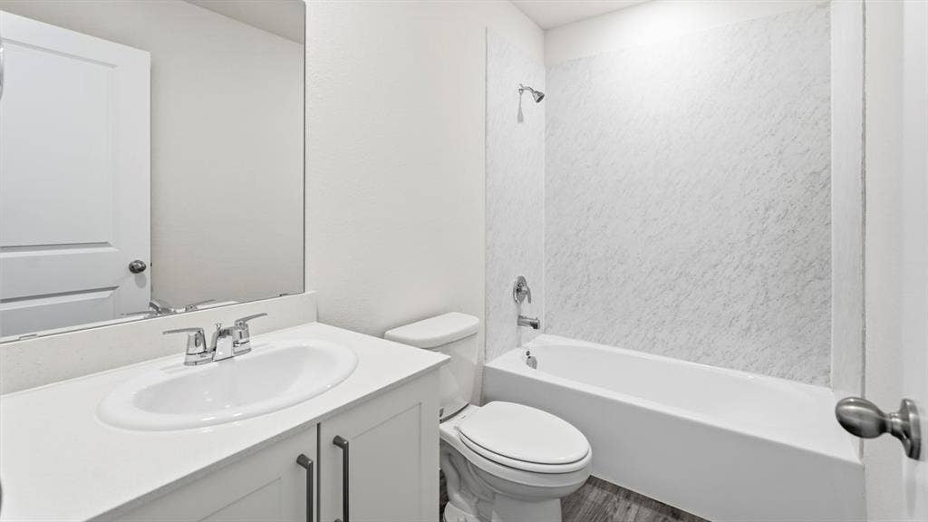 Bathroom featuring a single vanity with an integrated sink, polished chrome faucet, and a spacious bathtub with a textured surround