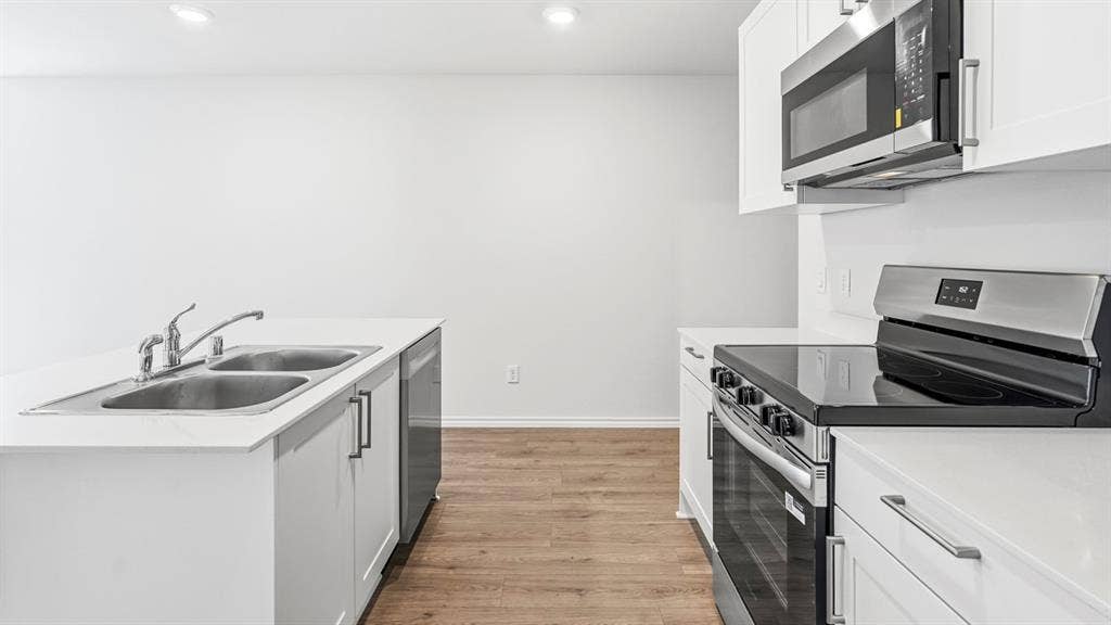 Modern kitchen featuring white cabinetry, light countertops, wood-finish flooring, stainless steel appliances, and a double basin sink