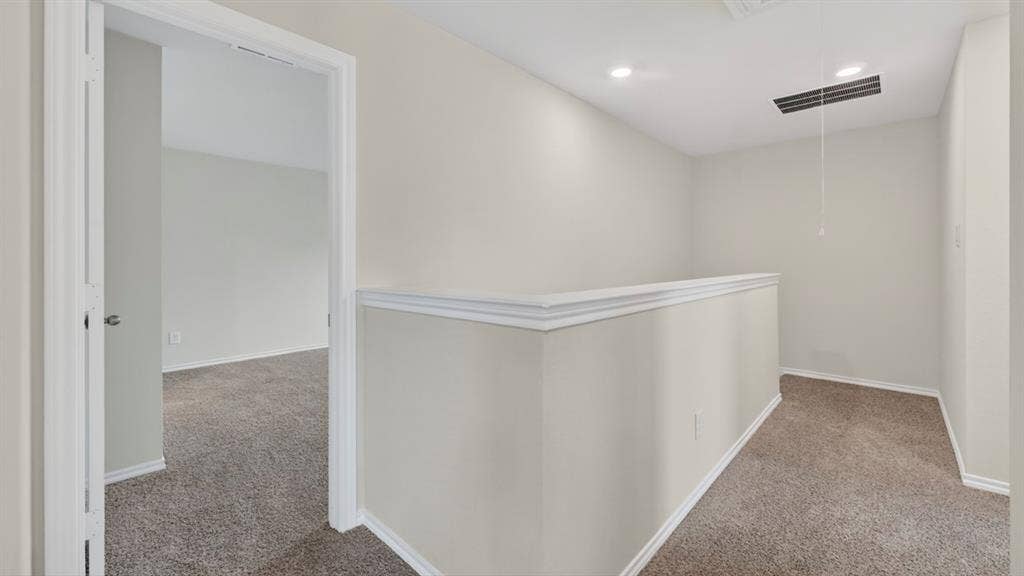 Carpeted upper-level landing featuring a white railing, recessed lighting, and access to additional rooms
