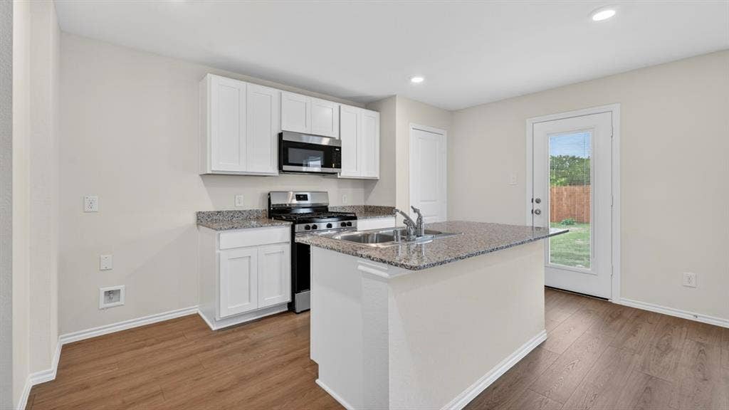 Modern kitchen showcasing white cabinetry, stainless steel appliances, and a central island with a double basin sink and granite-style countertop