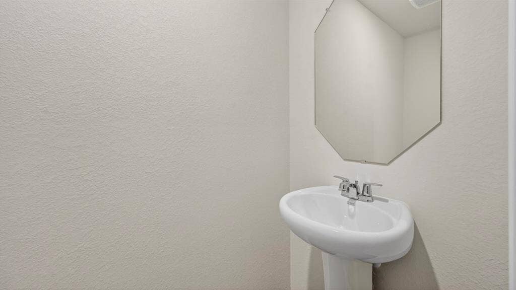 Pedestal sink with chrome faucet and an octagonal wall-mounted mirror