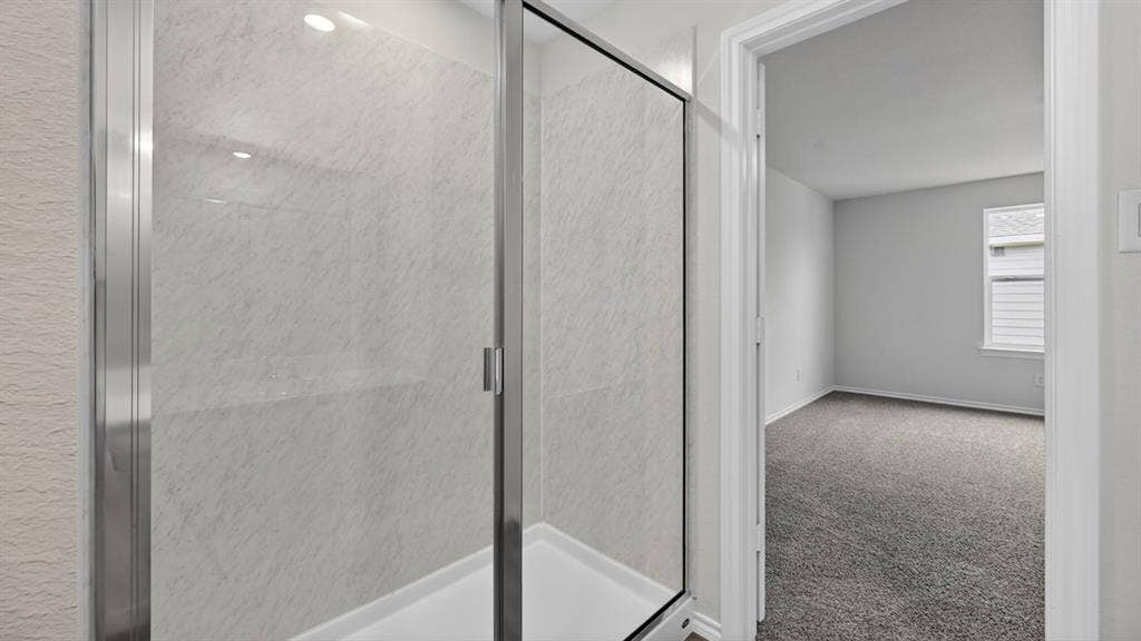 Walk-in shower with clear glass enclosure and light-toned, textured wall panels