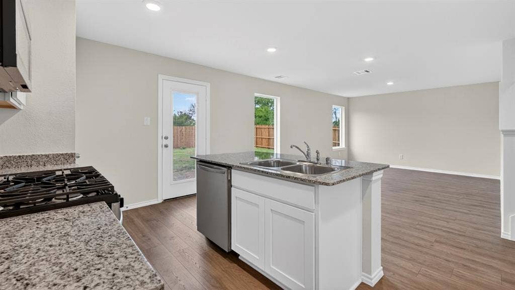 Kitchen island featuring a double basin stainless steel sink with a chrome faucet, granite countertops, and white cabinetry