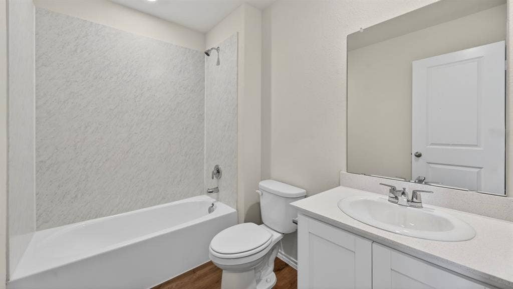 Bathroom featuring a white bathtub with a textured shower surround, chrome fixtures, a white vanity with an integrated sink, a large wall-mounted mirror, and wood-finish flooring