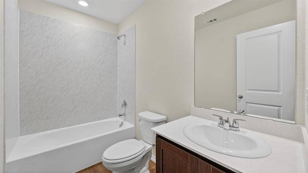 2825 Selfridge Lane, Forney, TX 75126 White bathtub with a textured shower surround, vanity with an integrated sink and light-toned countertop, dark wood-finish cabinet, and a large wall-mounted mirror