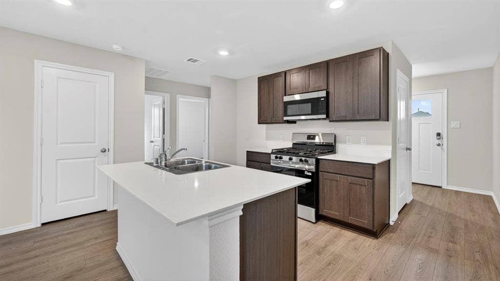 2825 Selfridge Lane, Forney, TX 75126 Kitchen featuring an island with a double basin sink, white countertops, dark wood-finish cabinetry, stainless steel microwave, and gas range
