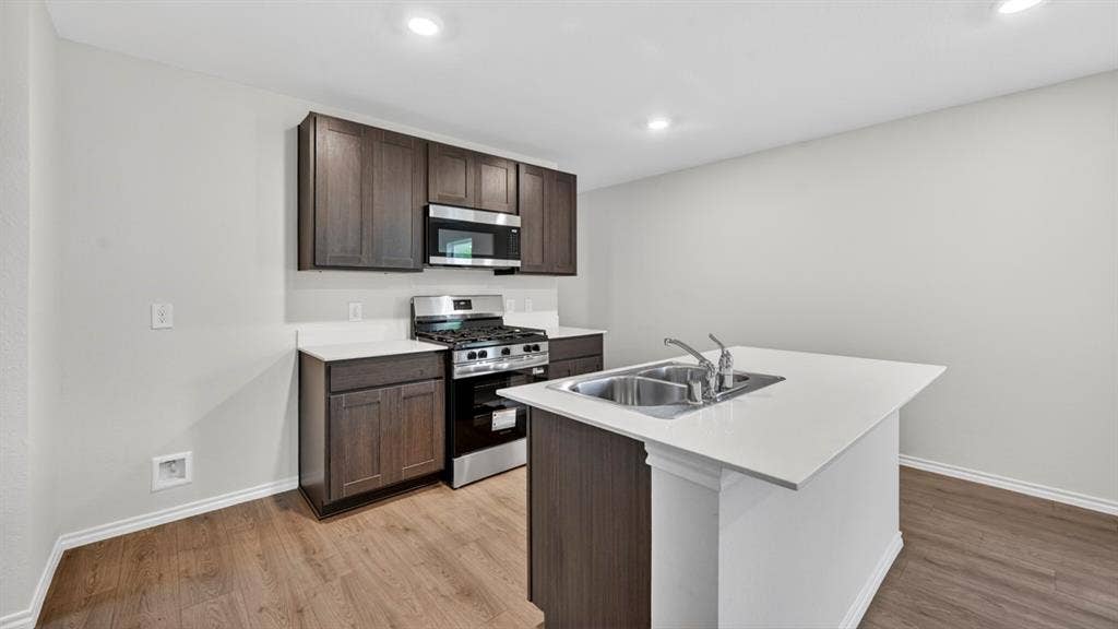 2825 Selfridge Lane, Forney, TX 75126 Kitchen featuring wood-finish flooring, dark wood-finish cabinetry, white countertops, stainless steel appliances, and a kitchen island with an integrated double sink