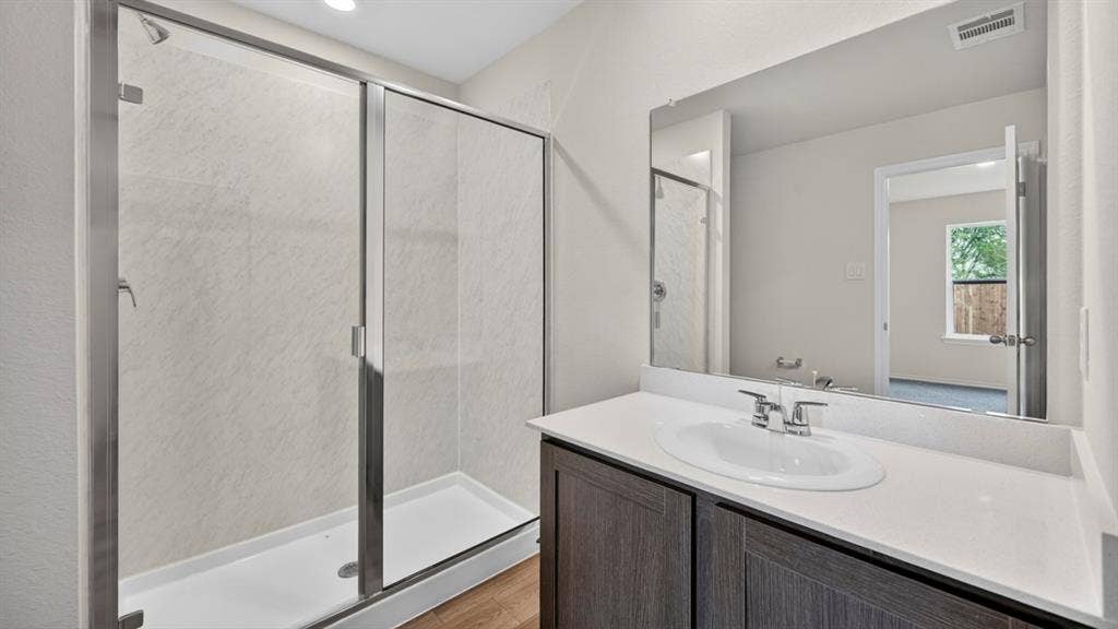 2825 Selfridge Lane, Forney, TX 75126 Walk-in shower with sliding glass door, single vanity with integrated sink, quartz-finish countertop, and wood-finish cabinetry