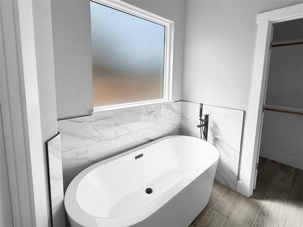 3025 Red Oak Drive, Granbury, TX 76048 Freestanding soaking tub with matte black fixtures, large-format tile surround, frosted privacy window, and wood-finish flooring