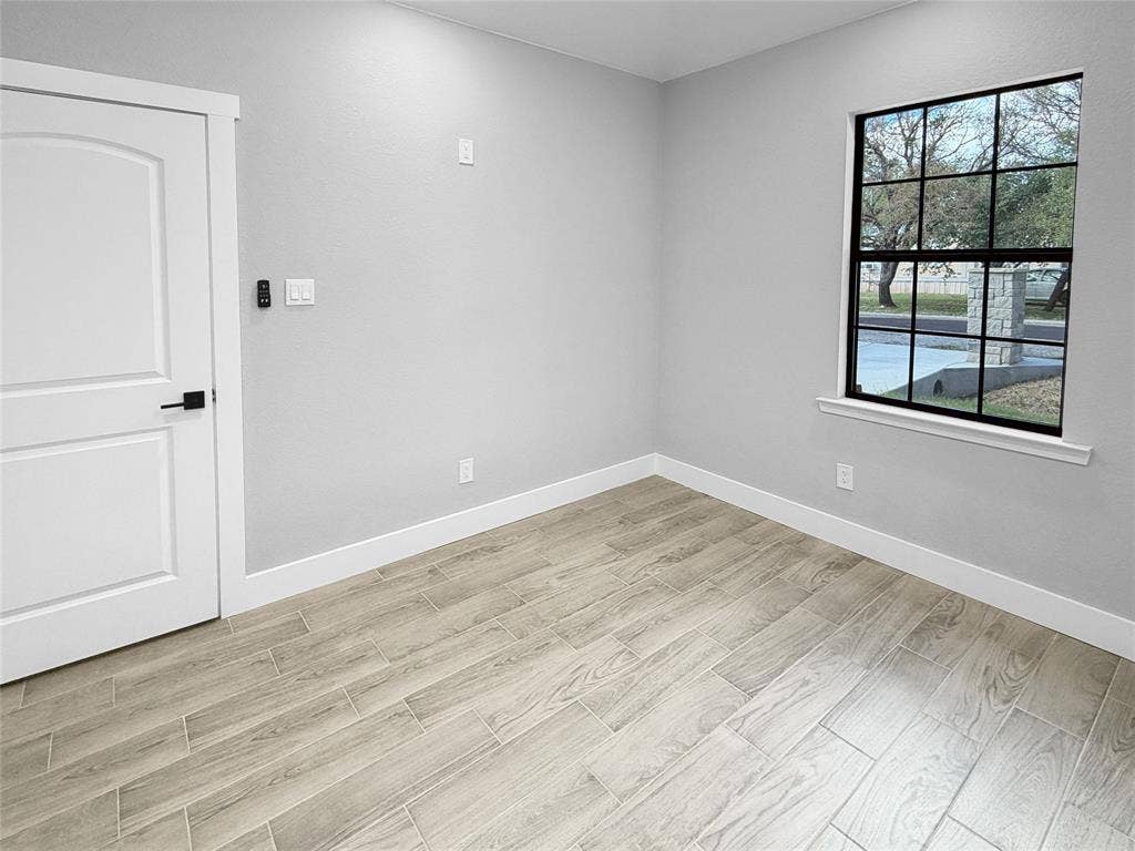 3025 Red Oak Drive, Granbury, TX 76048 Wood-finish flooring, neutral wall tones, multi-pane window with black framing, and a white arched-panel door with matte black hardware
