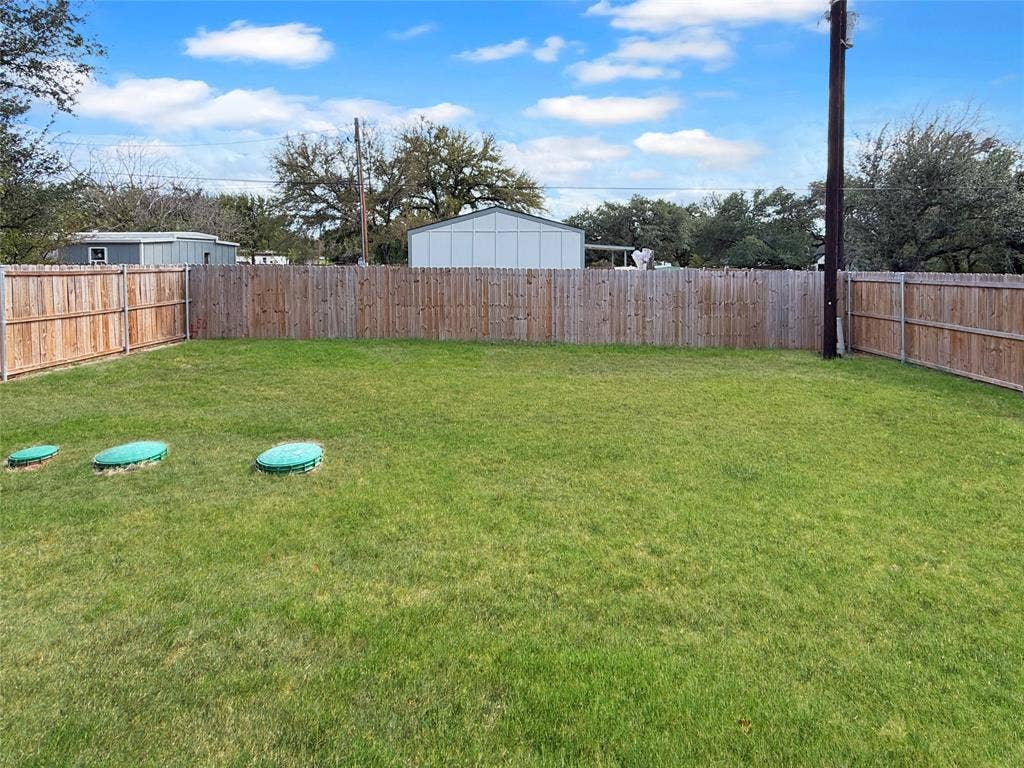 3025 Red Oak Drive, Granbury, TX 76048 Level grassy backyard featuring a wood privacy fence and mature trees