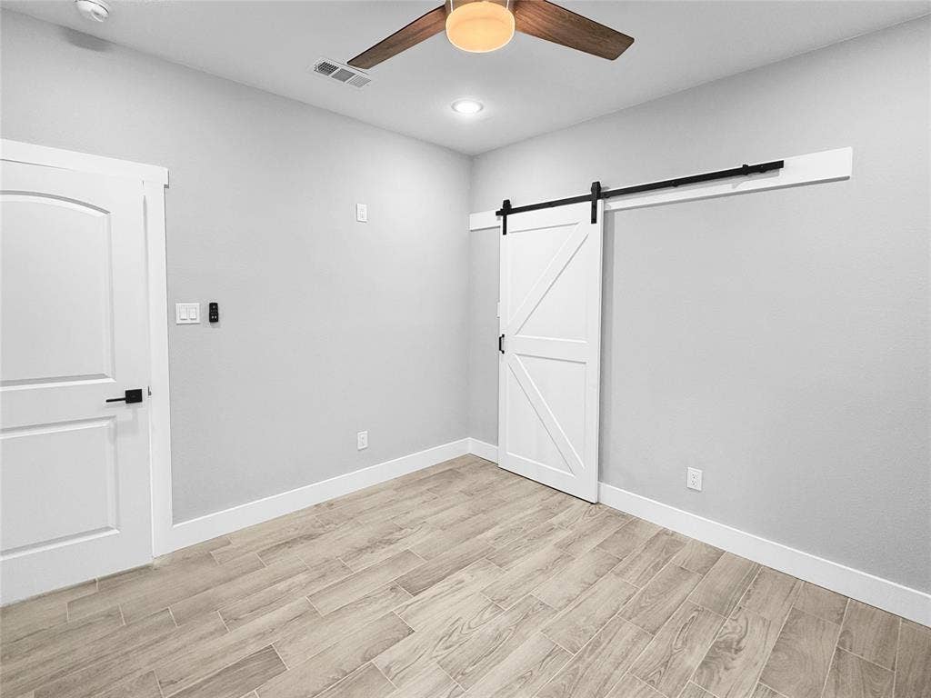 3025 Red Oak Drive, Granbury, TX 76048 Interior space featuring wood-finish tile flooring, a white paneled sliding barn door with matte black hardware, and a ceiling fan with integrated lighting