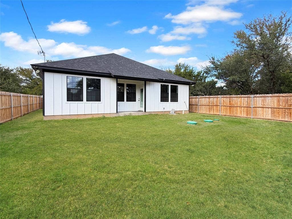 3025 Red Oak Drive, Granbury, TX 76048 Backyard featuring a grass lawn, full-perimeter wood privacy fencing, board-and-batten siding, and a hipped roof