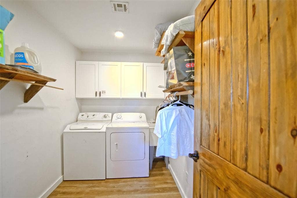 325 & 321 Grassy Way, Elm Mott, TX 76640 Laundry space featuring wood-finish flooring, white cabinetry, open wooden shelving, and a natural wood door