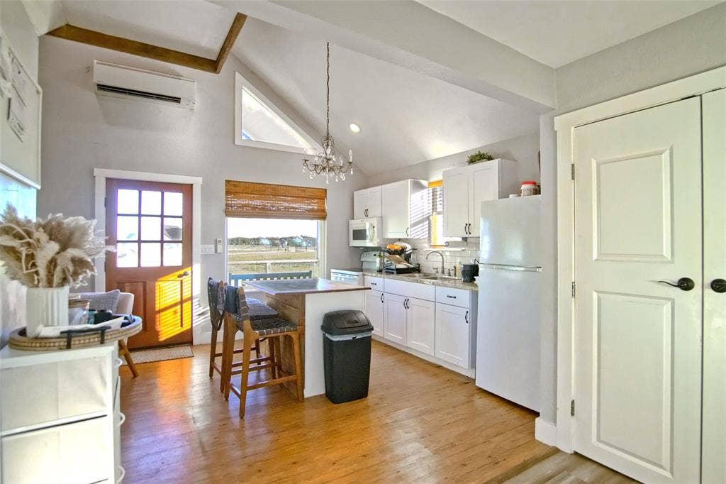 325 & 321 Grassy Way, Elm Mott, TX 76640 Kitchen featuring white cabinetry, vaulted ceilings with wood-beam detailing, a central island with wood-finish trim, a mounted ductless mini-split system, and a multi-pane wood-finish exterior door
