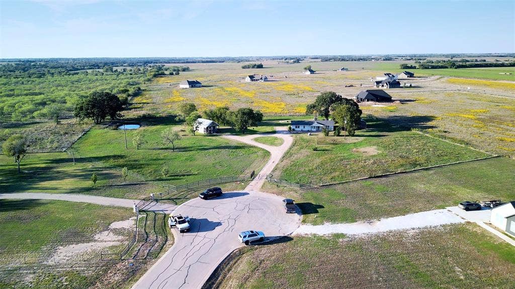 325 & 321 Grassy Way, Elm Mott, TX 76640 Aerial view of an expansive acreage property featuring a paved cul-de-sac entrance, gated perimeter fencing, mature trees, and an open grass pasture
