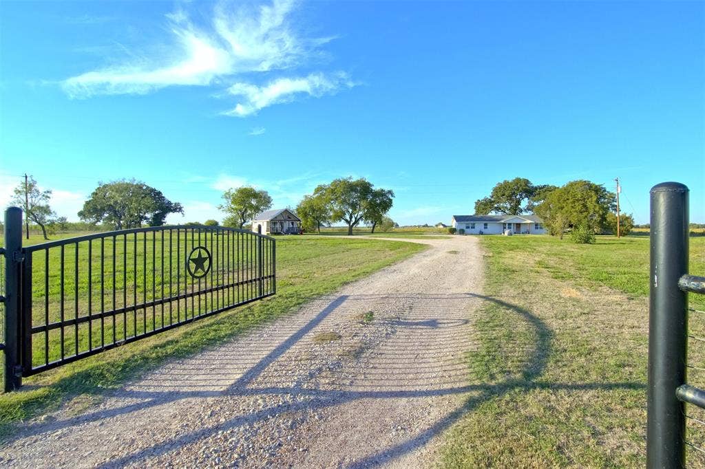 325 & 321 Grassy Way, Elm Mott, TX 76640 Gated entry featuring a decorative star motif and wrought-iron fencing, gravel driveway, and expansive acreage with mature trees