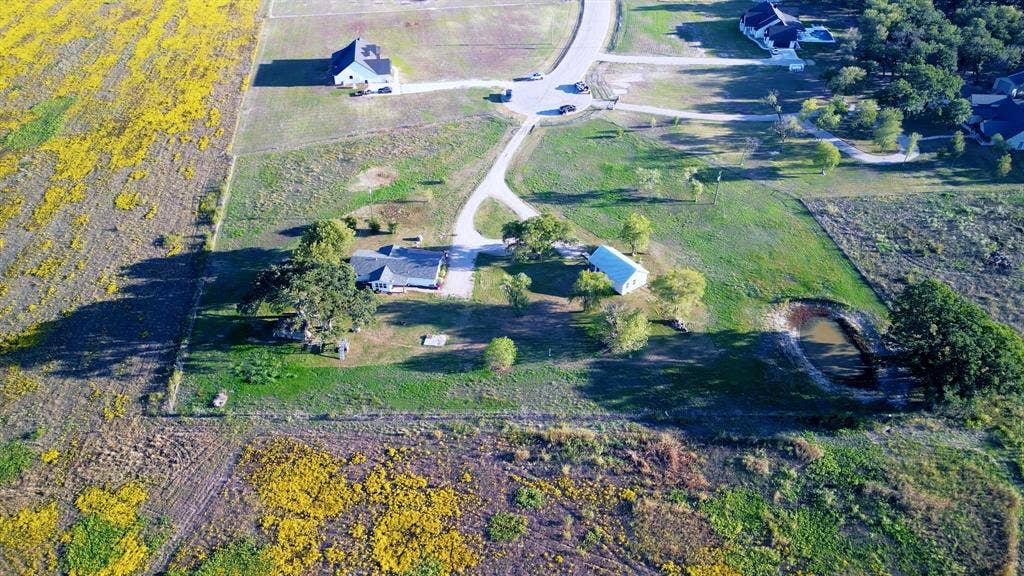 325 & 321 Grassy Way, Elm Mott, TX 76640 Aerial perspective featuring an expansive lot, paved driveway, detached structure, mature trees, and an on-site pond