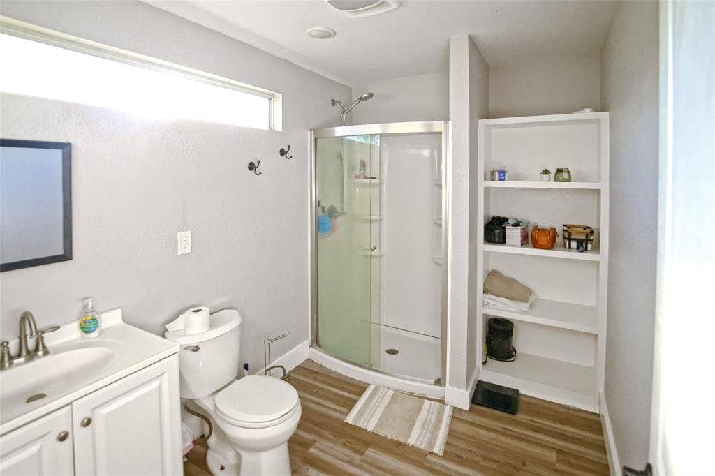 325 & 321 Grassy Way, Elm Mott, TX 76640 Bathroom featuring wood-finish flooring, a white vanity cabinet with an integrated sink, a glass-enclosed corner shower, built-in recessed shelving, and a clerestory window