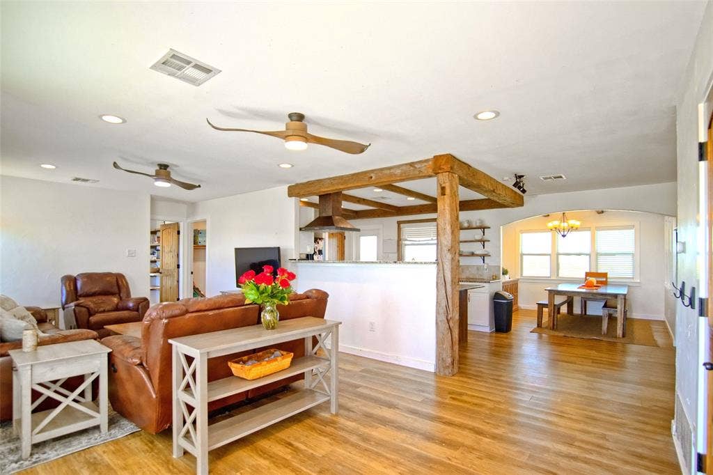 325 & 321 Grassy Way, Elm Mott, TX 76640 Open-concept interior featuring wood-finish flooring, exposed timber support beams, a stainless steel range hood, recessed lighting, and an arched entryway